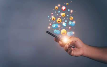 Hands holding and typing to communicate with others through emoji emotion. Online social communication,Social media,emotion, hearts. Chat Conversation on mobile. Man working using chatting applicationの写真素材