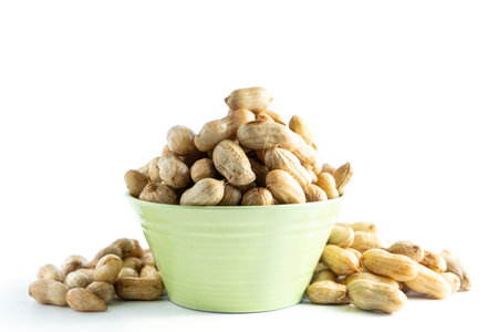 A light green bowl overflowing with roasted peanuts in the shell, isolated on a clean white background. Healthy snack or ingredient.の写真素材