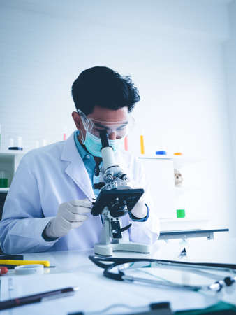 Asian male scientist Is working seriously Chemistry experiment With looking at the microscope In the laboratory, the color tone image.の写真素材
