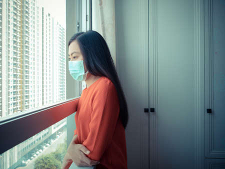 A woman wearing a mask Standing in the room and looking out the window, close-up.の写真素材