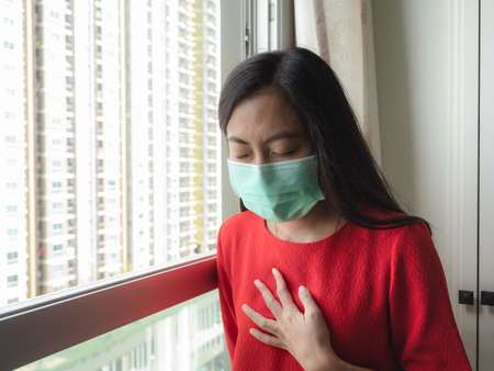 A woman wearing a mask Standing in the room and looking out the window, close-up.の写真素材