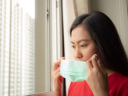 A woman wearing a mask Standing in the room and looking out the window, close-up.の写真素材