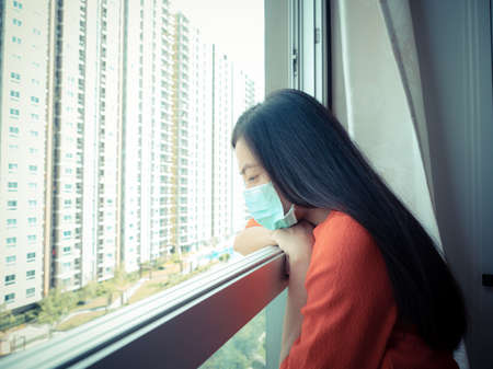 A woman wearing a mask Standing in the room and looking out the window, close-up.の写真素材