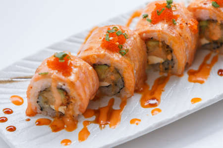 Torched Salmon Maki Sushi with Shrimp Tempura, Avocado and Cheese inside. Topping with Sauce, Ebiko (Shrimp Egg) and Scallion.の写真素材