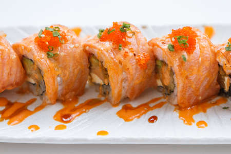 Torched Salmon Maki Sushi with Shrimp Tempura, Avocado and Cheese inside. Topping with Sauce, Ebiko (Shrimp Egg) and Scallion.の写真素材
