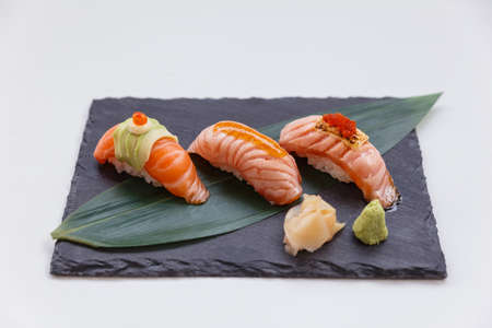 Torched and Raw Salmon Sushi Set Topping with Avocado, Mayonnaise and Ikura, Sauce and Cheese with Ebiko Served with Wasabi and Prickled Ginger on Black Stone Plate.の写真素材