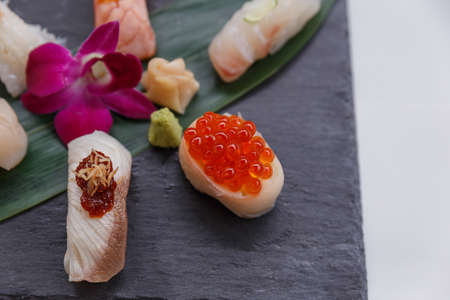 Sushi Set Include Torched Salmon, Engawa, Hotate, Hamachi, Tai and Ikura with Hirame Served with Wasabi and Prickled Ginger on Leaf on Black Stone Plate.の写真素材