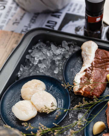 Beef, Pork, and Scallop Preparing for Cooking on Iced Plate with Olive Oil, Wine, Half of Onion and Black Pepper on Newspaper.の写真素材
