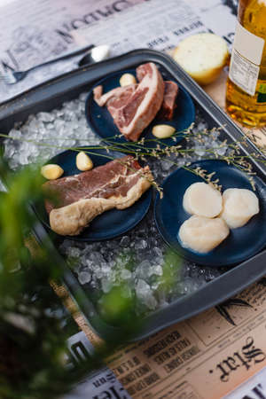 Beef, Pork, and Scallop Preparing for Cooking on Iced Plate with Olive Oil, Wine, Half of Onion and Black Pepper on Newspaper.の写真素材