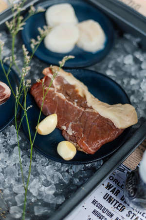 Beef, Pork, and Scallop Preparing for Cooking on Iced Plate with Olive Oil, Wine, Half of Onion and Black Pepper on Newspaper.の写真素材