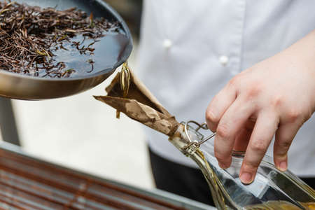 Chef Pouring Rosemary Oil From Pan in The Glass Bottle with Paper Cone.