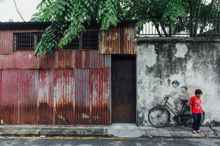 Painted Girl and Boy Riding Real Bicycle on The Old Concrete Wall from The Street of George Town. Penang, Malaysia.のeditorial素材