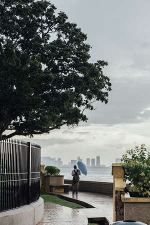 Raining in Park that near the Coast with a Man Holding Umbrella and Seeing Seascape and Cityscape of George Town, Penang, Malaysia.の写真素材