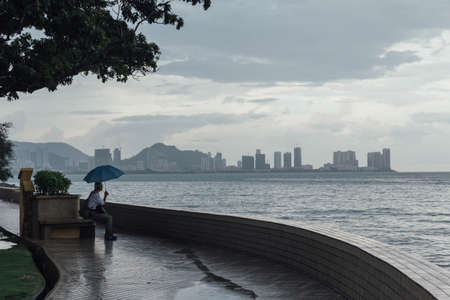Raining in Park that near the Coast with a Man Holding Umbrella and Seeing Seascape and Cityscape of George Town, Penang, Malaysia.の写真素材