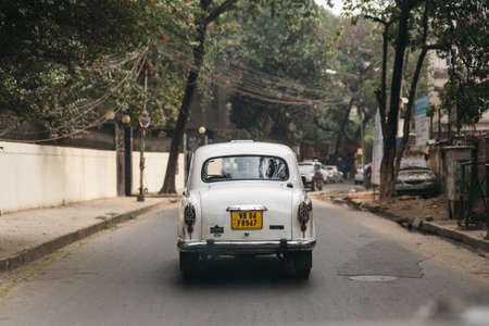 White classic car run on the street with trees in Kolkata, Indiaのeditorial素材
