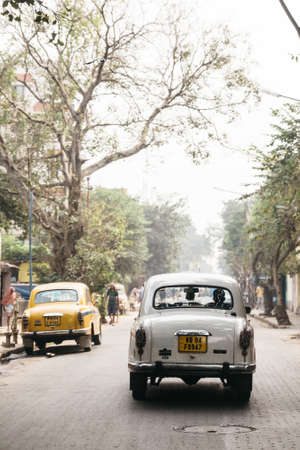 White classic car run on the street with trees in Kolkata, Indiaのeditorial素材