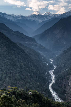 Kangchenjunga mountain with clouds above. Among green hills with concrete fortress and river that...