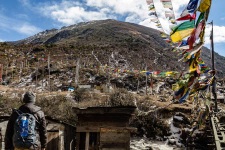 Tourist stand in the front of outdoor toilet with Tibetan prayer flags with Black mountain with snow on the top is background at Thangu and Chopta valley in winter in Lachen. North Sikkim, India.の写真素材
