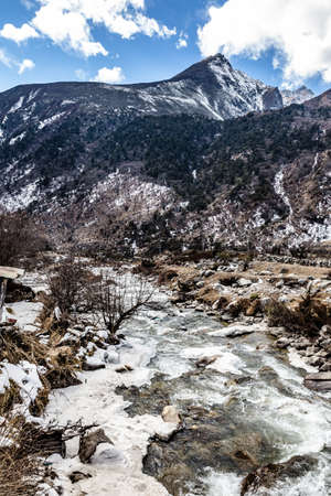 Landscape with black mountain with snow on the top. On the ground is frozen river with stone, ice and yellow grass at Thangu and Chopta valley in winter in Lachen. North Sikkim, India.の写真素材