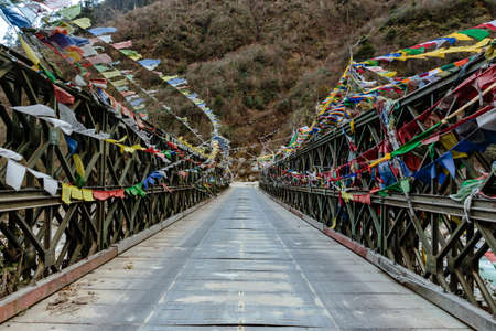 Tibetan prayer flags swaddled with bridge over frozen river with Black mountain with snow on the top is background at Thangu and Chopta valley in winter in Lachen. North Sikkim, India.の写真素材