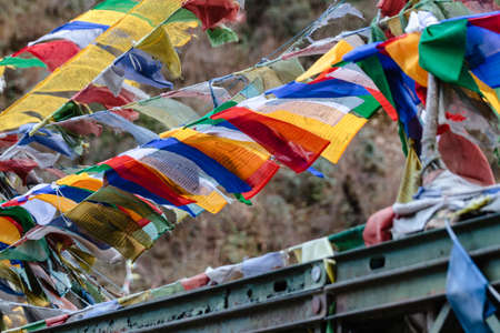 Tear colorful Tibetan prayer flags waving and swaddled with bridge over frozen river at Thangu and...