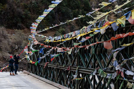 Couple tourists with tear colorful Tibetan prayer flags waving and swaddled with bridge over frozen river at Thangu and Chopta valley in winter in Lachen. North Sikkim, India.のeditorial素材