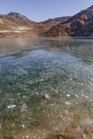 Frozen pond with ice on the frozen surface with brown mountain and clear sky in the background in winter in Tashi Delek near Gangtok. North Sikkim, Indiaのeditorial素材