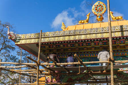 Golden Dharma wheel with deer in the top of entrance gate with construction site and workers of Guru Rinpoche Temple at Namchi. Sikkim, India.の写真素材