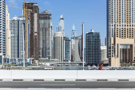 City scape with modern high-rise buildings, street and with man walking in walk way and blue sky in background at Dubai.のeditorial素材