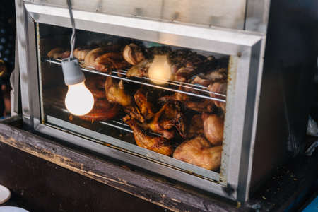 Roasted chicken in electric oven with light bulb at food market near Kew Mae Pan in Chiang Mai, Thailand.の写真素材
