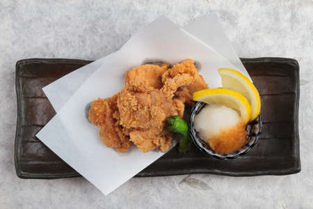 Close-up Japanese deep fried Chicken (Karaage) with cooking paper served with tempura sauce (Tentsuyu) mixing mince radish and sliced of lemon in black plate on washi (Japanese paper).の写真素材