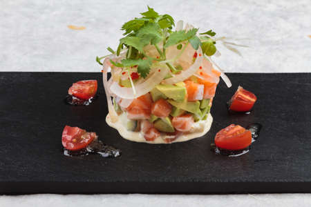 Close-up Diced salmon salad with avocado, tomato, onion, chilli, and coriander served in black rectangle stone plate on washi (Japanese paper).の写真素材