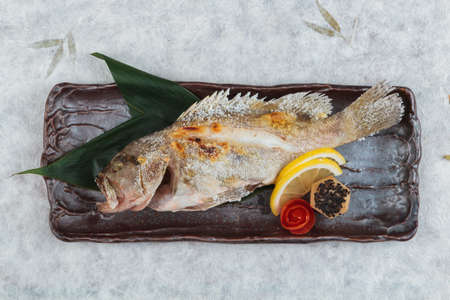 Top view of Salt-Grilled Snapper (Shioyaki) served with sliced lemon and tomato on stone plate on...