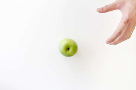 Top view of Moving left hand for grabbing a green apple on white background.の写真素材