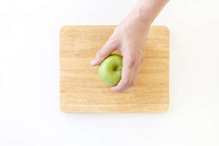 Top view of Left hand grab a green apple in wooden chopping board on white background.の写真素材