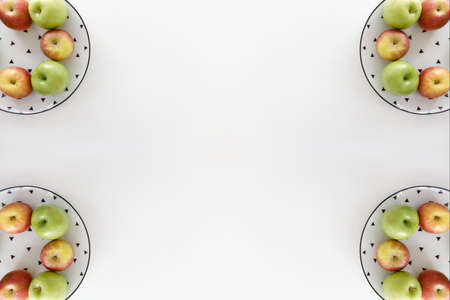 Top view of Red and green apples in white plate with black triangles pattern on the four corners with white background.の写真素材