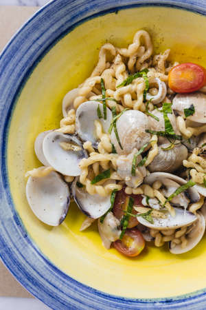 Fusilli Avellinesi pasta with clams and tomato in yellow and blue plate.