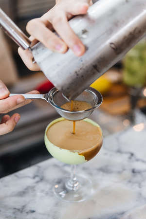 Bartender gently pour coffee mix with alcohol pass the filter in wine glass with green paste for...