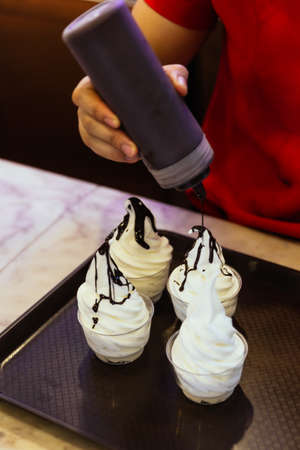 Four cups of vanilla soft serve ice cream topping with chocolate sauce at the cafe in Hanoi, Vietnam.の写真素材