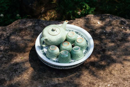 Light green ceramic tea set including jar, cups and plate on stone table under tree shadow  at Ham Rong Mountain Park in Sa Pa, Vietnam.の写真素材