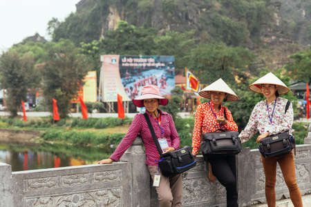 Women photographers wearing conical hat waiting for tourists to take a photo near Trang An with mountain in the background in summer in Ninh Binh, Vietnam.のeditorial素材