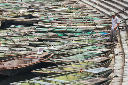Man walking from land to the boat in area of boat stop over the river with many empty row boats in summer at Trang An Grottoes in Ninh Binh, Vietnam.のeditorial素材