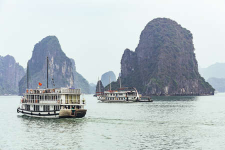 Cruising tourist boat over emerald water with towering limestone islands in the background in summer at Quang Ninh, Vietnam.のeditorial素材