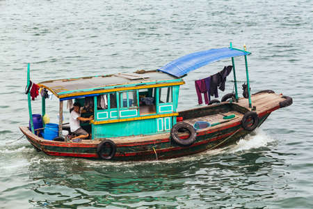 Small fishing boat over emerald water with towering limestone islands in the background in summer at Quang Ninh, Vietnam.のeditorial素材