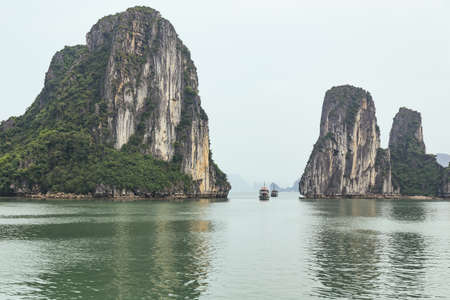 limestone islands on left and right side over emerald water with tourist boats cruising pass defile...