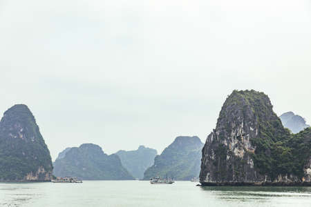 Seascape with towering limestone islands over emerald water with growing trees on it that view from cruising tourist boat in summer at Quang Ninh, Vietnam.の写真素材
