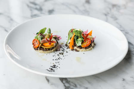 Quinoa canapes topping with pan seared asparagus, tomato and baby vegetables and olive oil served on white plate.の写真素材