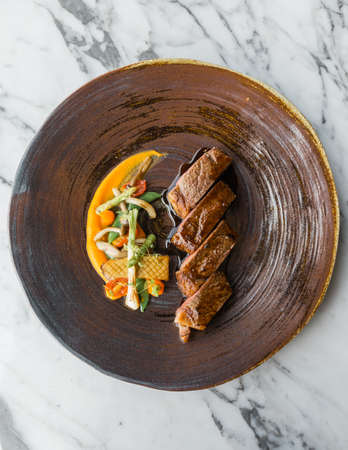 Top view of roasted medium rare wagyu beef served with sour sauce with roasted baby vegetables on stone plate.の写真素材