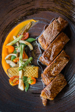 Roasted medium rare wagyu beef served with sour sauce with roasted baby vegetables on stone plate.の写真素材