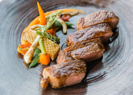 Roasted medium rare wagyu beef served with sour sauce with roasted baby vegetables on stone plate.の写真素材